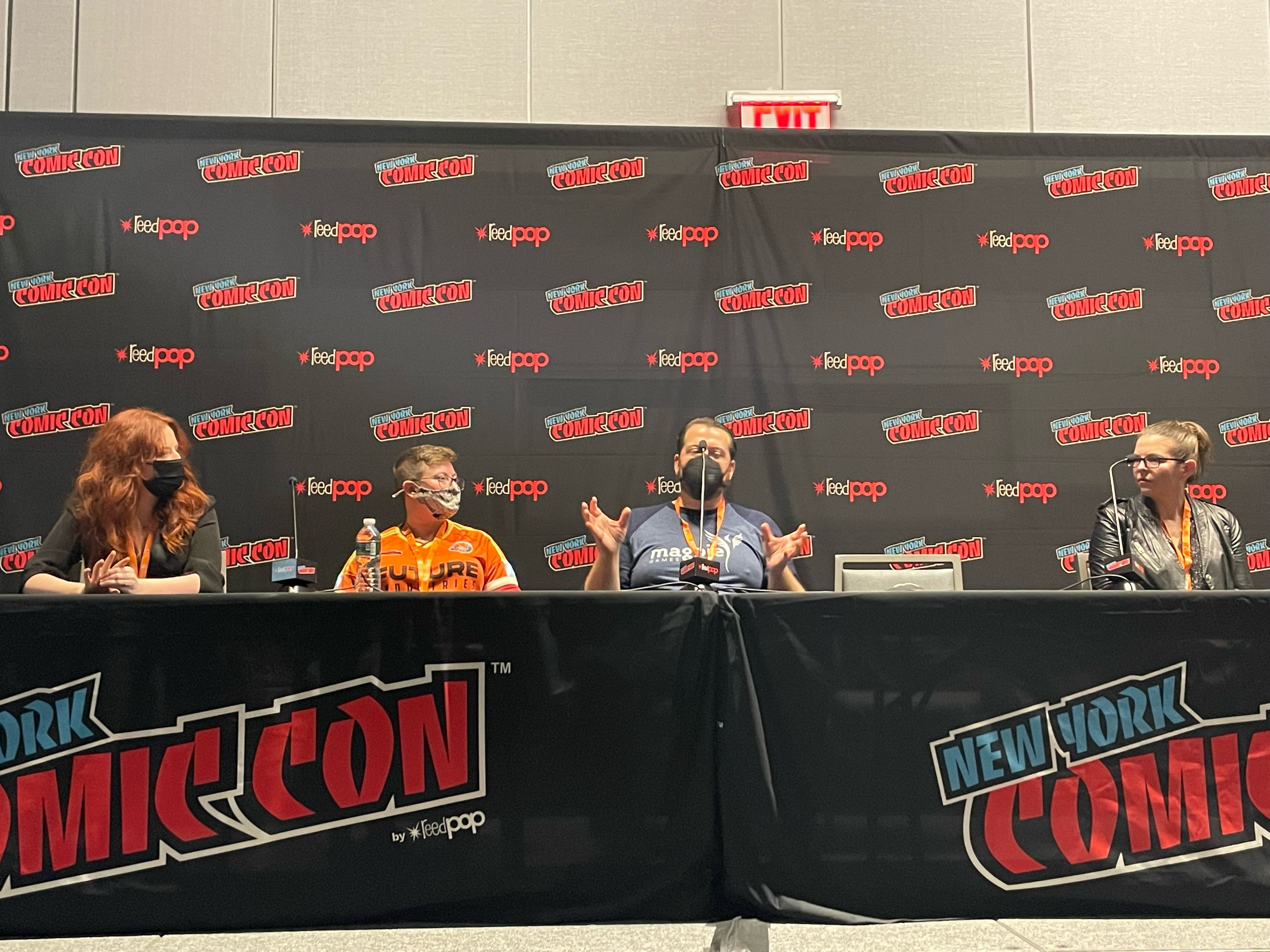 Panelists sitting in front of microphones in front of a NYCC background